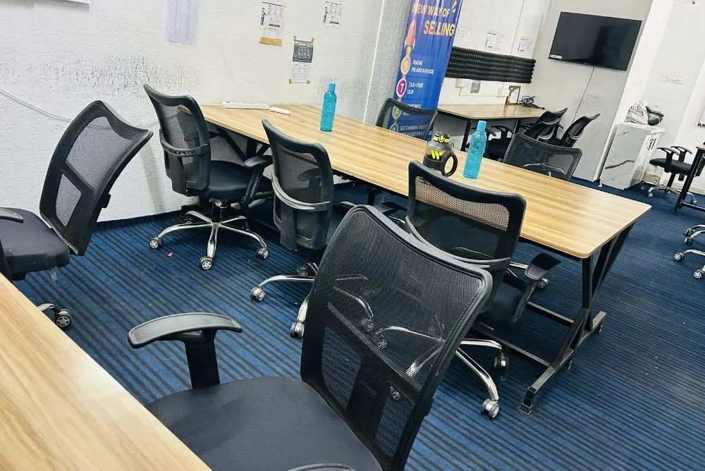 Modern coworking space for freelancers featuring long wooden desks, black mesh chairs, and blue striped carpeting.