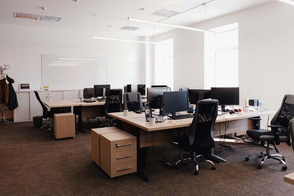 A formal traditional office featuring rows of dark desks, ergonomic chairs, a whiteboard, and neutral decor.