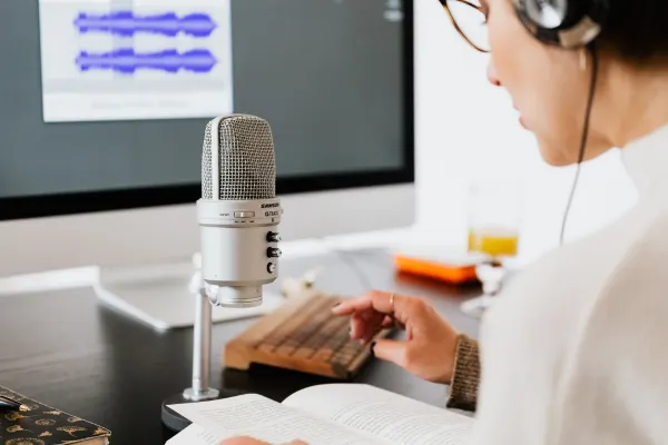 Close-up view of a person editing audio on computer with professional microphone in foreground during podcast production.