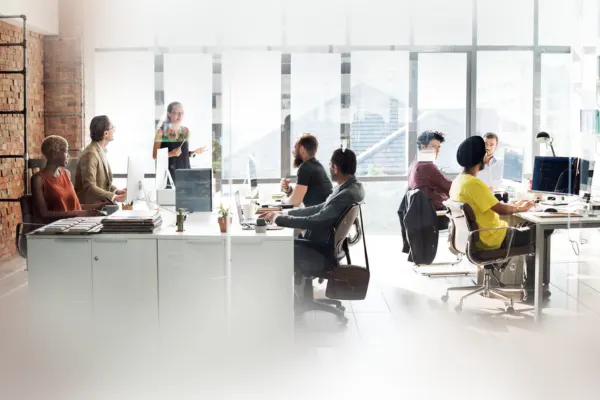 A diverse group of professionals working and collaborating at shared desks inside a bright, open-plan office space.