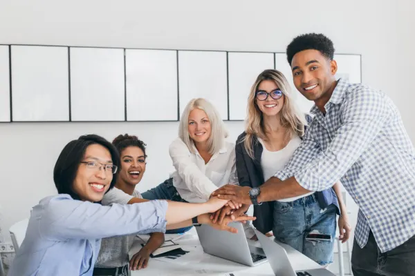 A diverse team of happy office colleagues smiling together and stacking their hands in a circle over a desk.