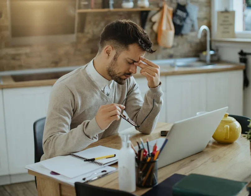 Tired man rubbing his eyes at a desk, a stark visual of how freelancers struggle with fatigue while working at home.
