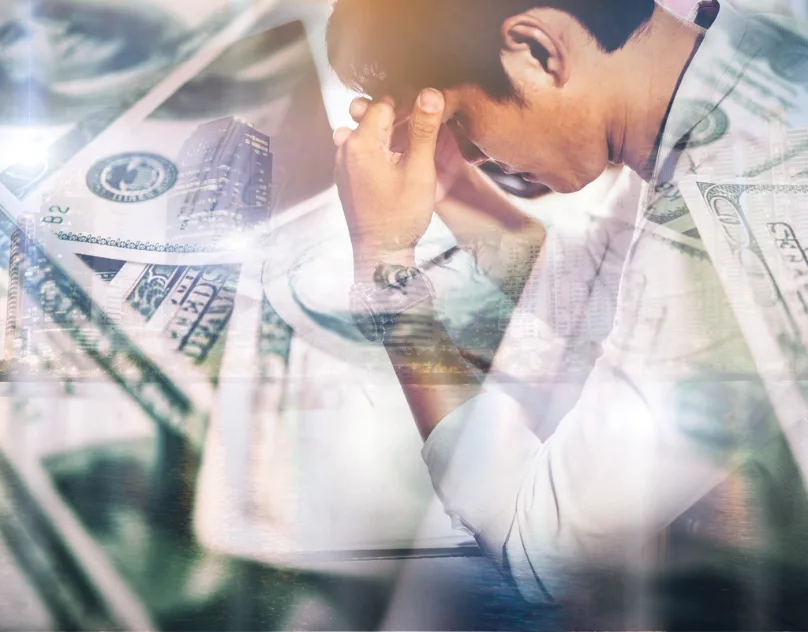 Stressed man holding his head over layered images of money, a common freelancers struggle with income instability