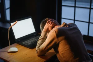 An exhausted worker holding his head in distress late at night, depicting severe remote work burnout symptoms.