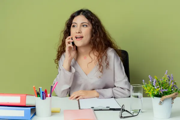 Young woman talking on her smartphone while seated at a desk stocked with colorful office supplies and notes.